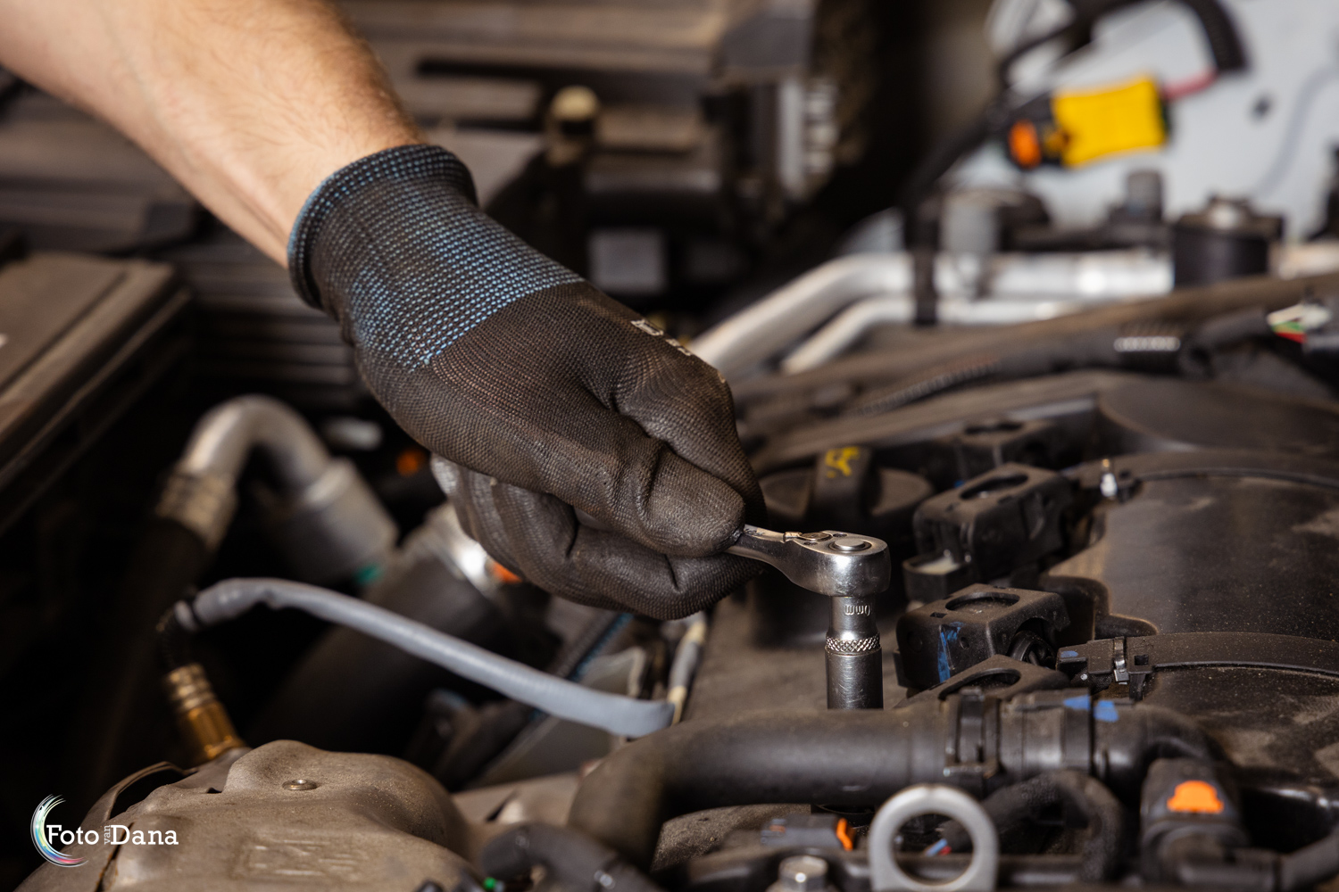 Detailopname van de handen van een autotechnicus tijdens het werken onder de motorkap in een professionele werkplaats, vastgelegd door een zakelijke fotograaf. Illustratie van het belang van kwalitatieve bedrijfsfotografie voor websites